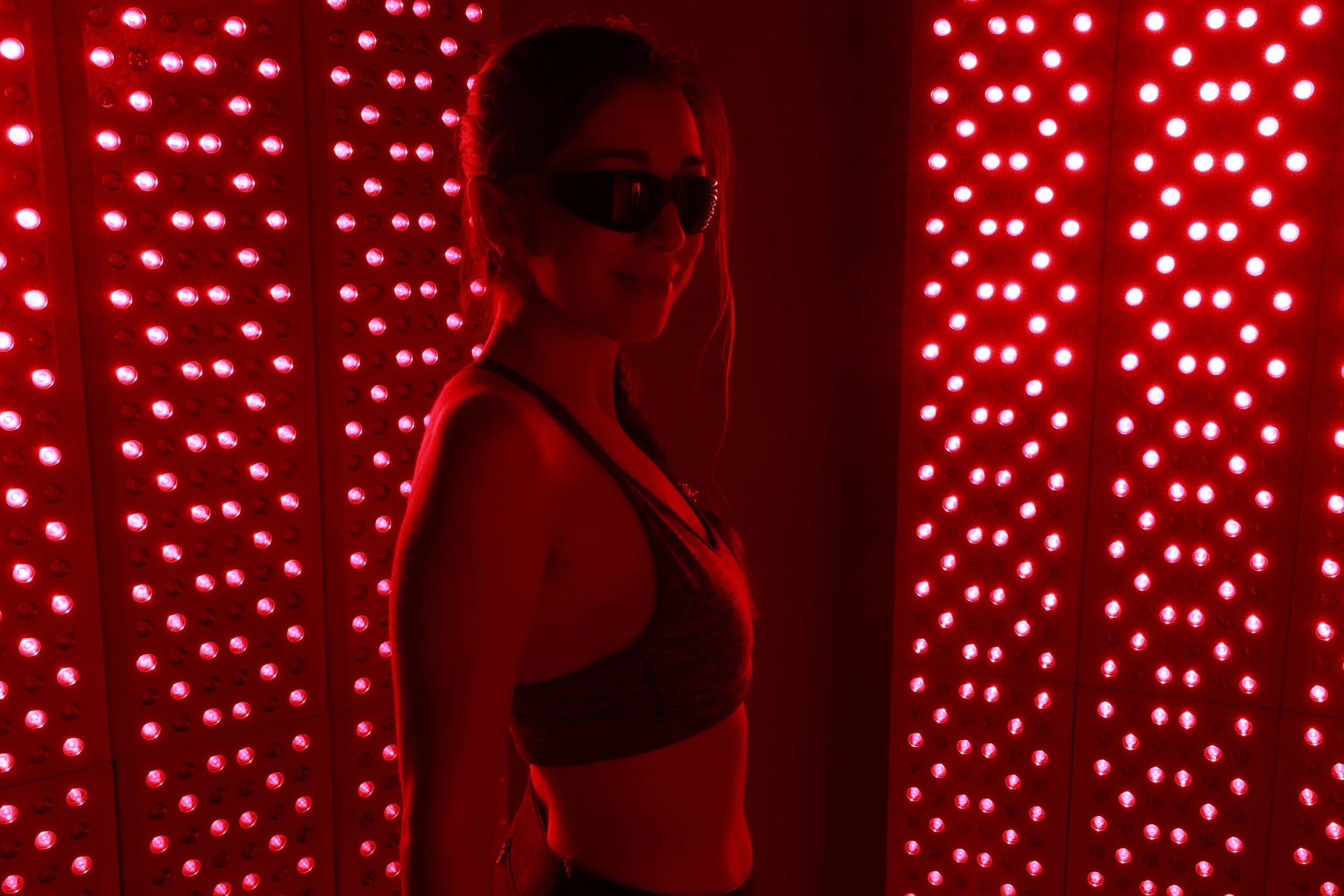 woman stands in front of two large red light panels with black glasses on.