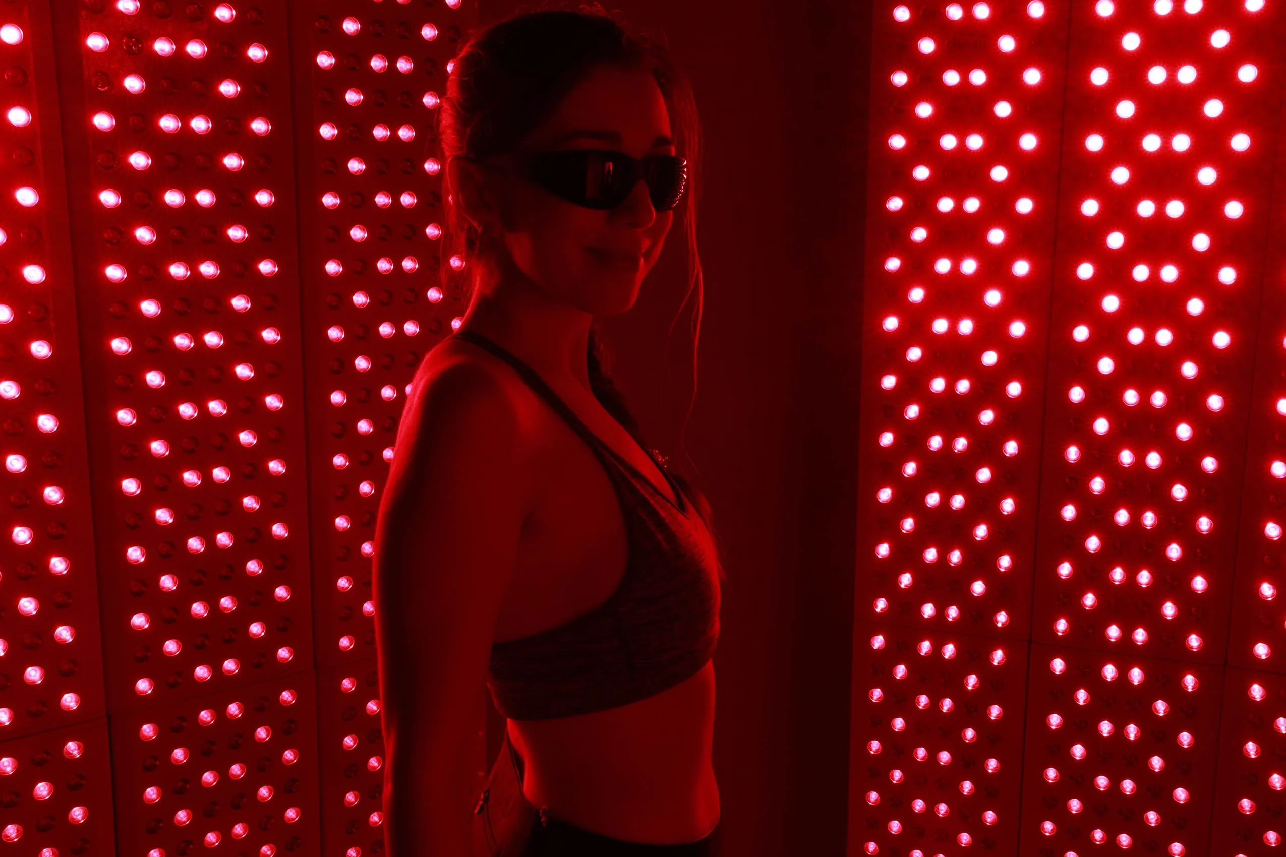 woman stands in front of two large red light panels with black glasses on.